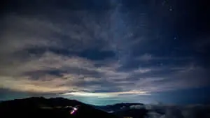 a mountain with clouds and stars above it