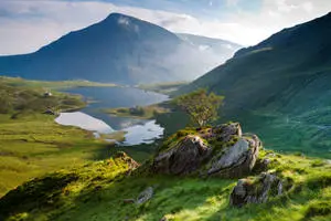 a green grassy hillside with a lake