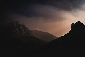 a mountain range with a sun shining through the clouds